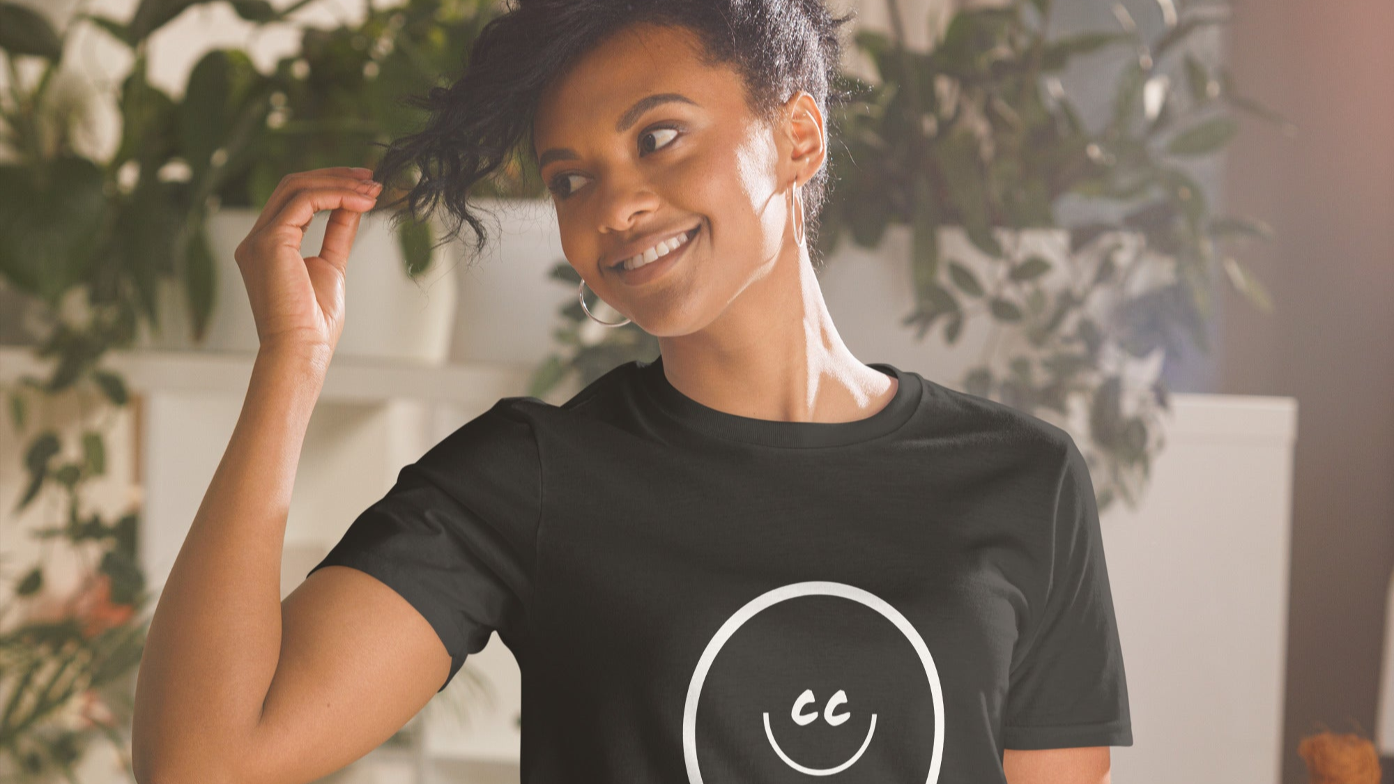 A smiling young lady wearing the CC THE LOVE Smile 001 black graphic t-shirt, a streetwear design created to encourage eye contact and human connection.